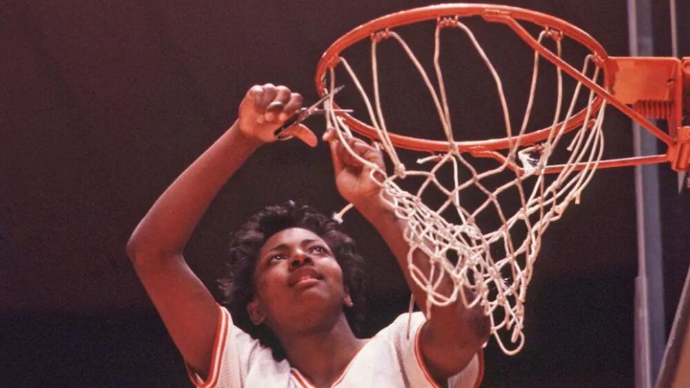 Fran Harris cuts down a basketball net, a tradition often associated with celebrating a significant victory in basketball. Harris is wearing a Texas Longhorns basketball jersey and is captured in the act of removing the net from the hoop.