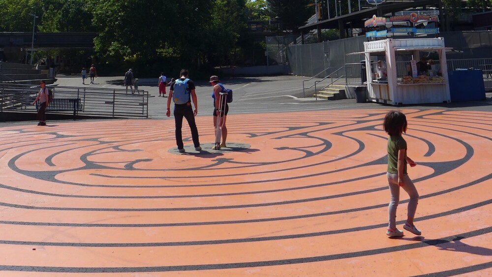 The Seattle Center Labyrinth is an orange flat labyrinth backdropped by the Space Needle