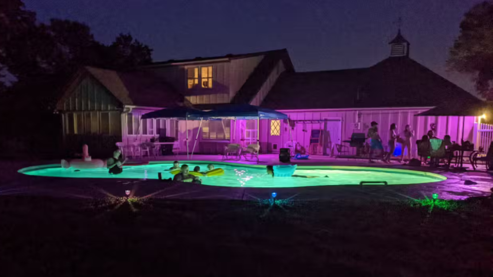 At night, a pool full of swimmers lit by colorful lights.
