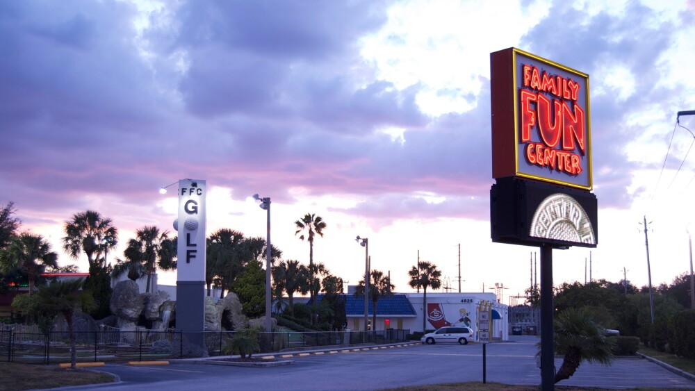 A mini golf sign is lit up in the darkening sky.