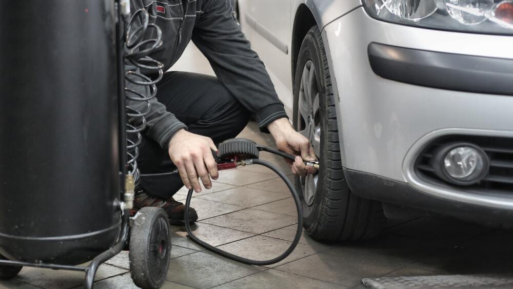 A person adding air to the tire of a sedan.