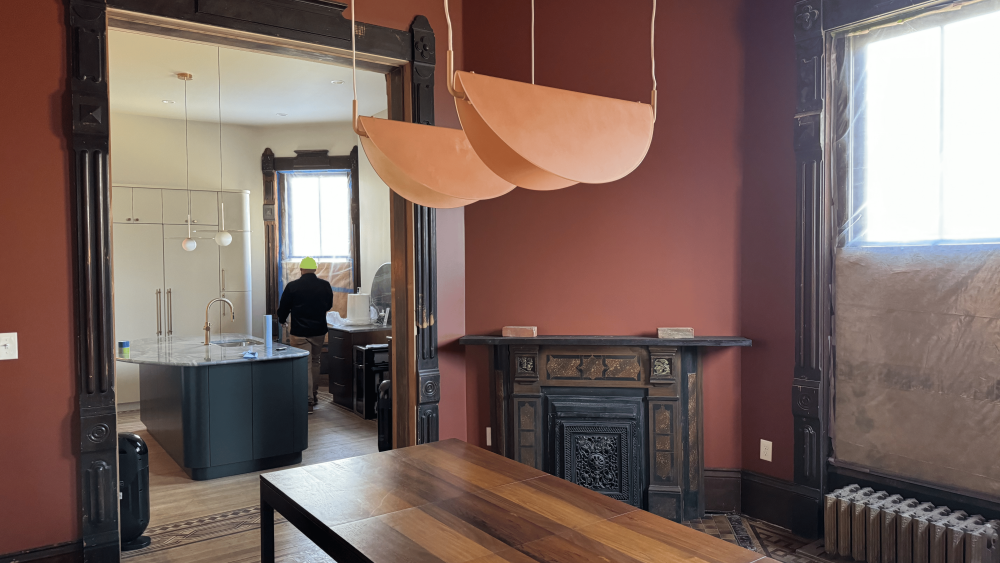 an interior of a dining room painted red with a wooden table, leading into a ktichen with an island.
