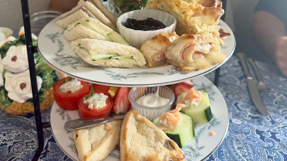 A three-tier tray of afternoon tea bites with sandwiches, cake, and vegetables