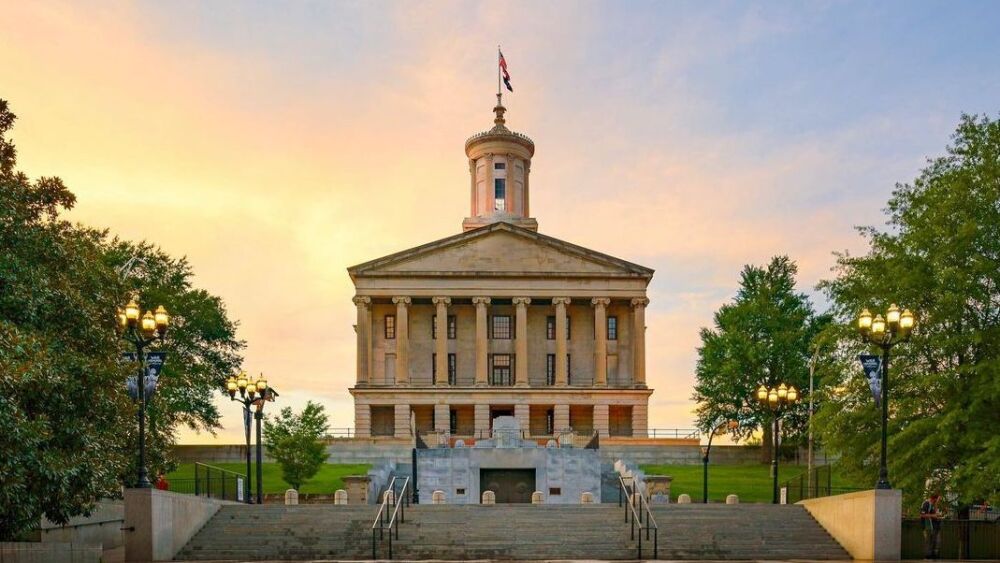 A straight forward photo of the capitol with orange and blue-colored skies in the background.