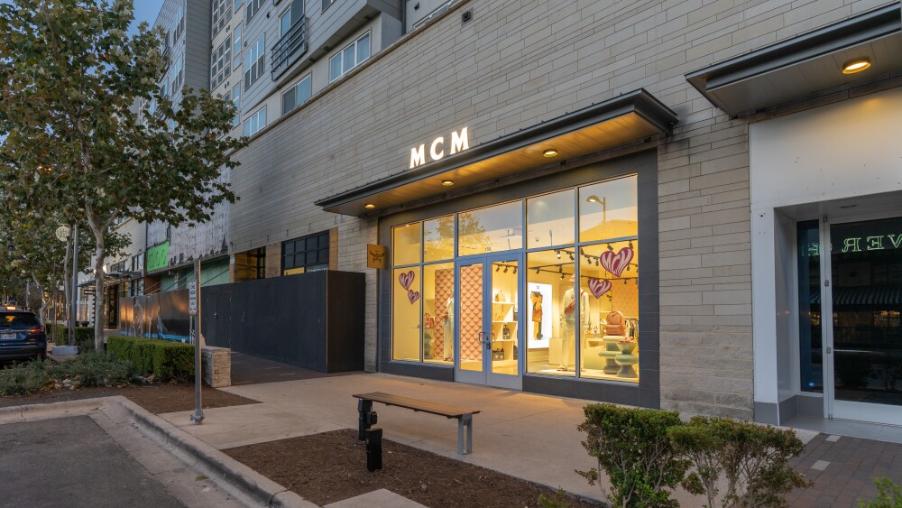 The MCM store as seen from the outside at dusk. The store name glows over a simple awning, and you can see brightly colored items inside the well-lit store.