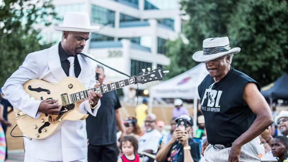 WStoday: Downtown Jazz in Winston-Salem showcasing man playing the guitar infront of the crowd and another man dancing next to him