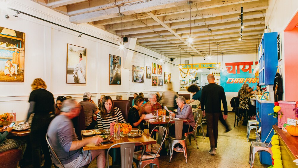 Lots of people sit at table's in Chai Pani's Asheville location. The movement of some of the individuals is blurred.