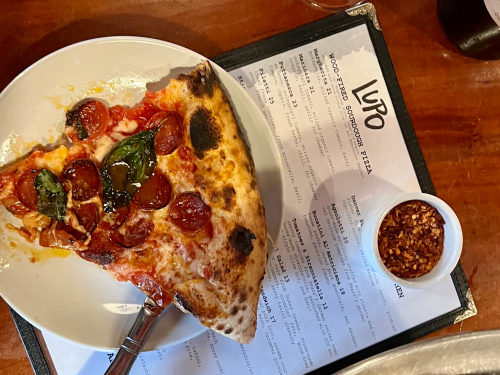 A slice of pizza on a plate sitting on a menu for Pizza Lupo