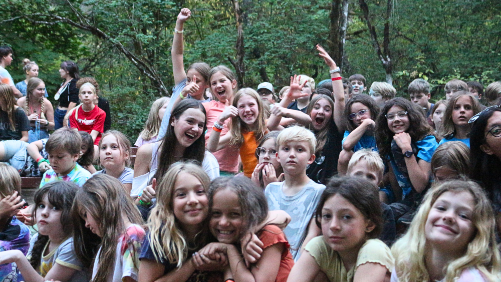 A large group of kids at summer camp posing for the camera in a playful way.