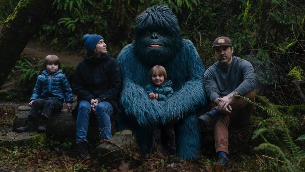 A family poses with a large blue ape creature in a verdant forest
