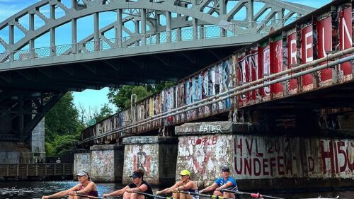 A team of four rowers going under the Boston University Bridge.