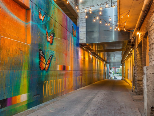 An alleyway decorated with string lights overhead and a colorful butterfly mural on the left wall.
