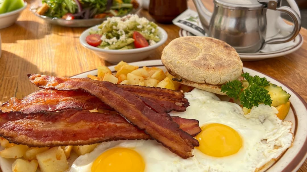 A breakfast plate from Hobee's with two sunnyside up eggs, bacon, potatoes, and an English muffin.