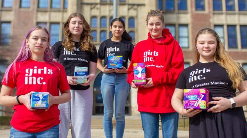 Five young women in Girls Inc garb stand in front of Madison East High School holding period products.jpg