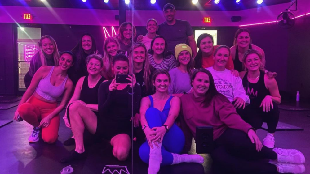 Workout group poses after a class in a dim light room that's illuminated by pink neon lights.
