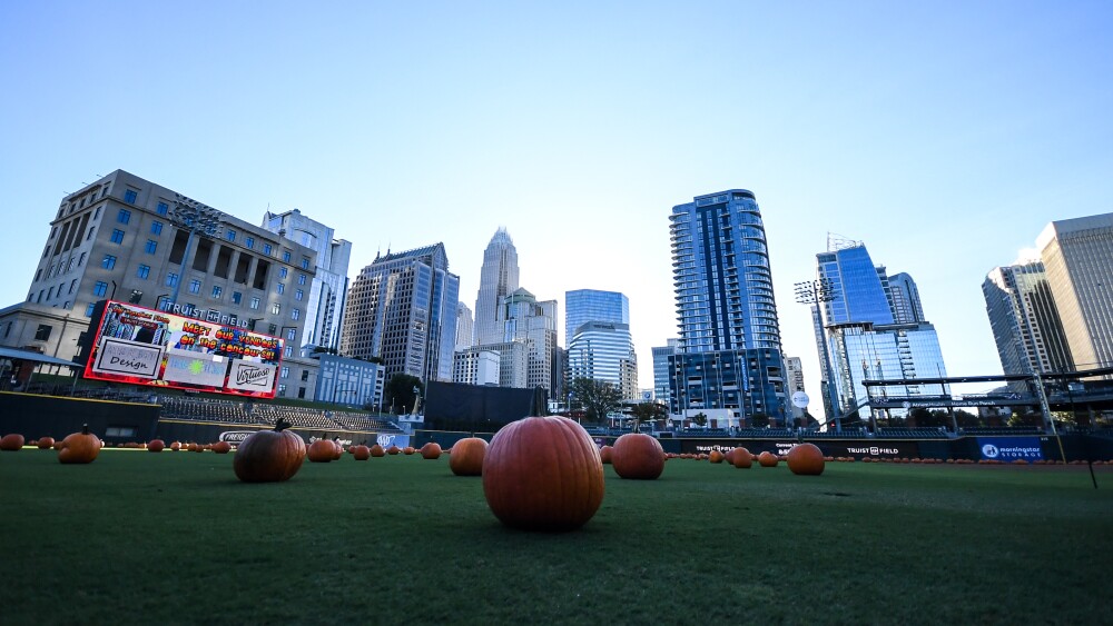 Pumpkins scattered about a baseball field with high-rise buildings in the background.