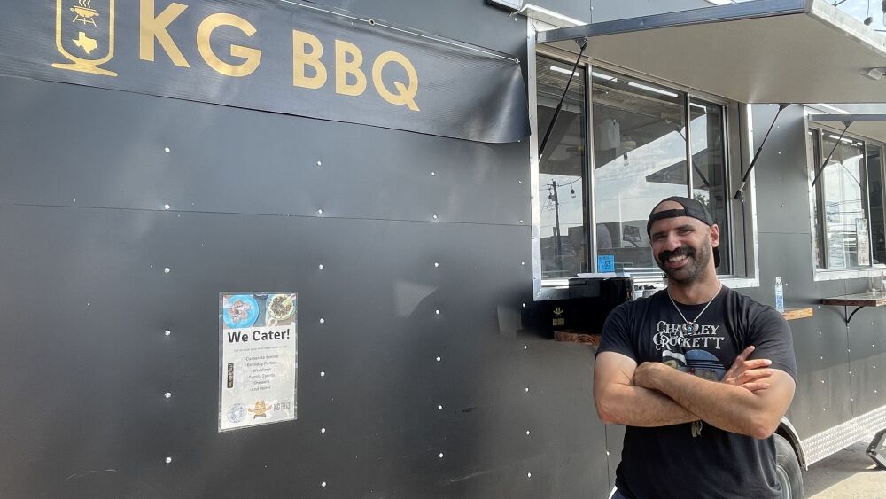 Kareem El-Ghayesh standing in front of his black barbecue food truck, KGBBQ.