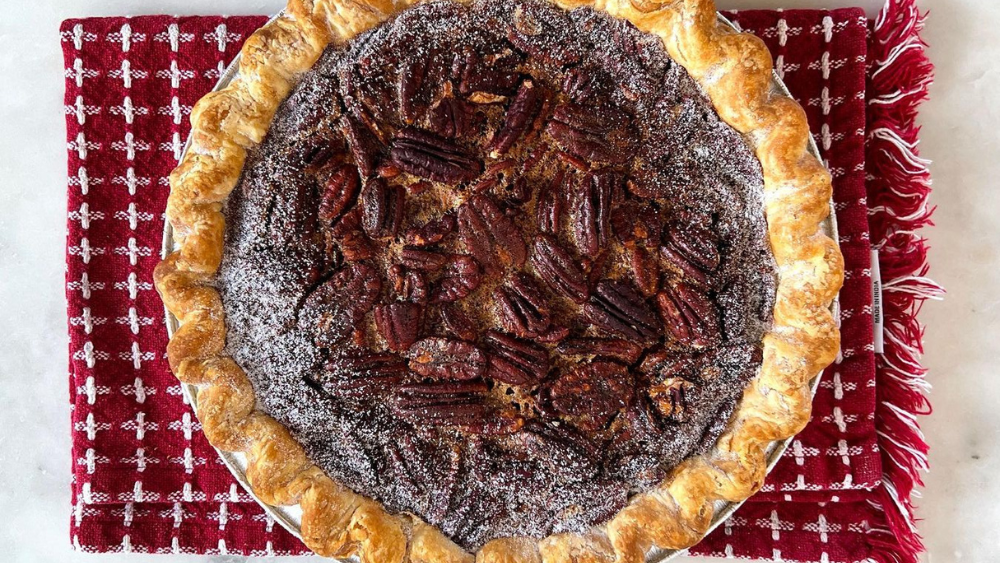 A pecan pie sits on a red kitchen towel.