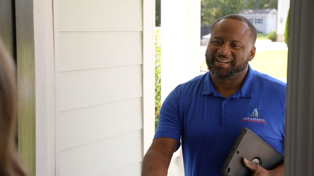 Man in blue, Air Experts branded polo greets a customer at the door to their home.