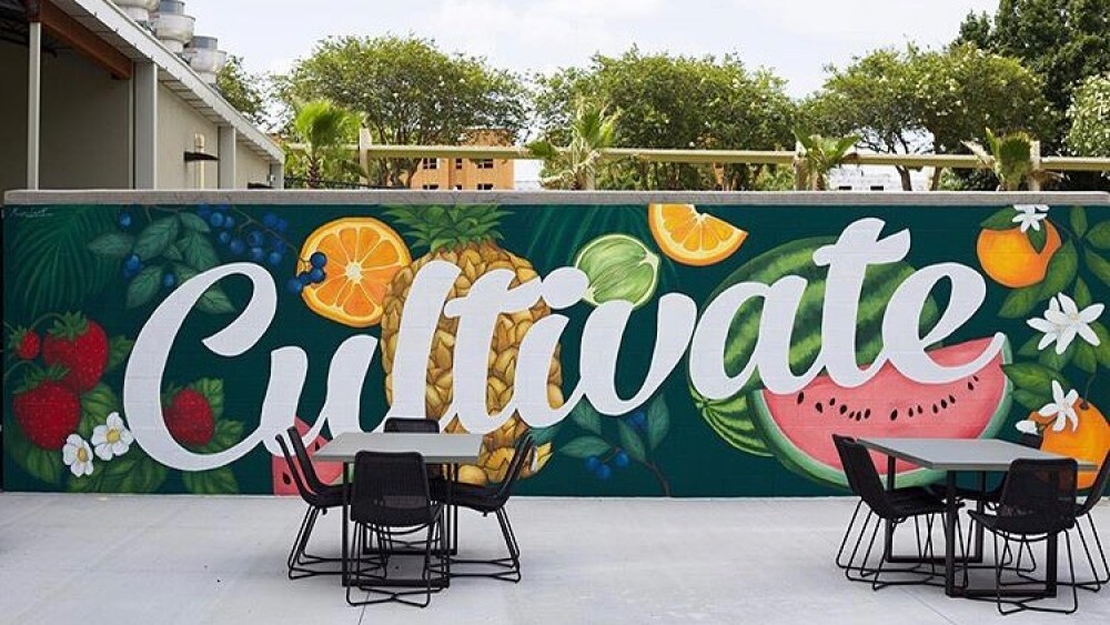 A green mural with various fruits and the word "Cultivate" overlooks patio tables