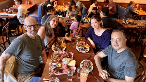 Two men and two women are seated at a table in a restaurant with plates of food in front of them. They're smiling at the camera.