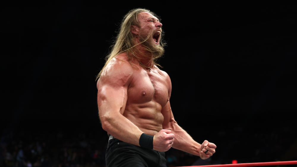 AEW star Big Bill, shirtless with long hair, stands in the ring, yelling with his fists clenched.
