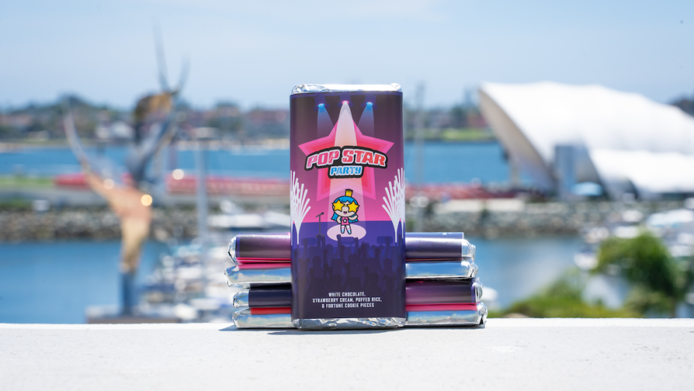 A chocolate bar wrapped in pink and purple packaging with the words "Pop Star Party" at the center and a cartoon character with stars for eyes.