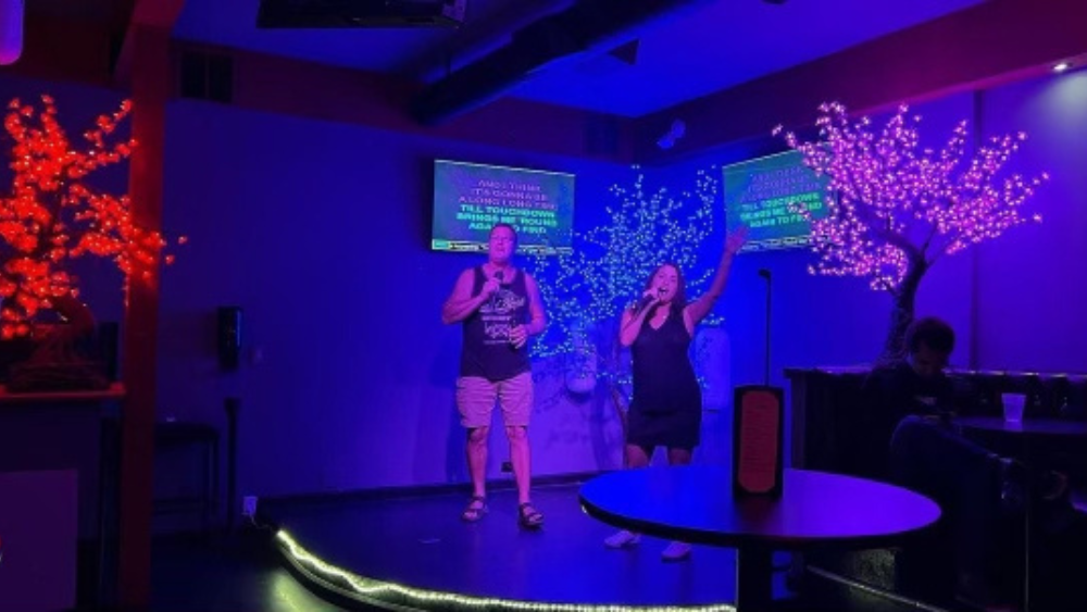 Two people duet karaoke under blue, purple, and red lights.