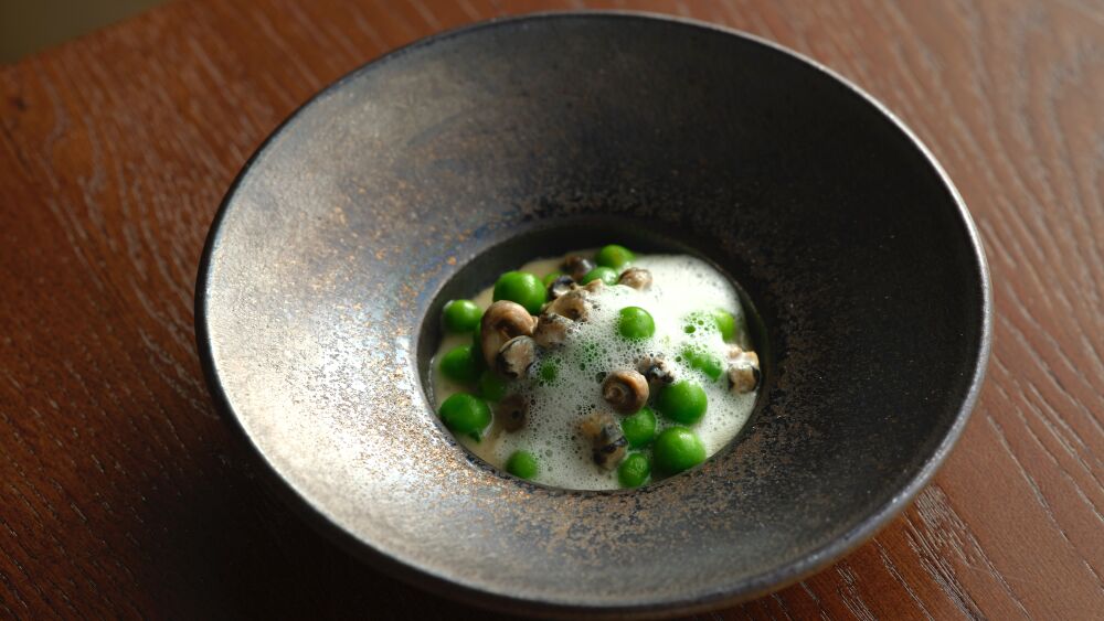 A plate of peas and foamy clams are served in a bowl on a restaurant table.