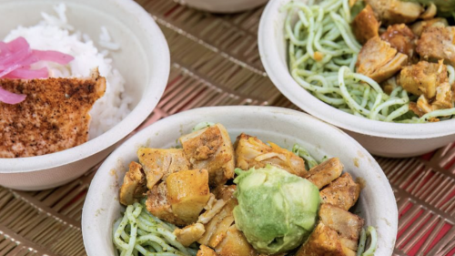 Several paper bowls filled with food sit atop a table. There are two different options, with one containing rice and salmon, and the other with chicken and green spaghetti.