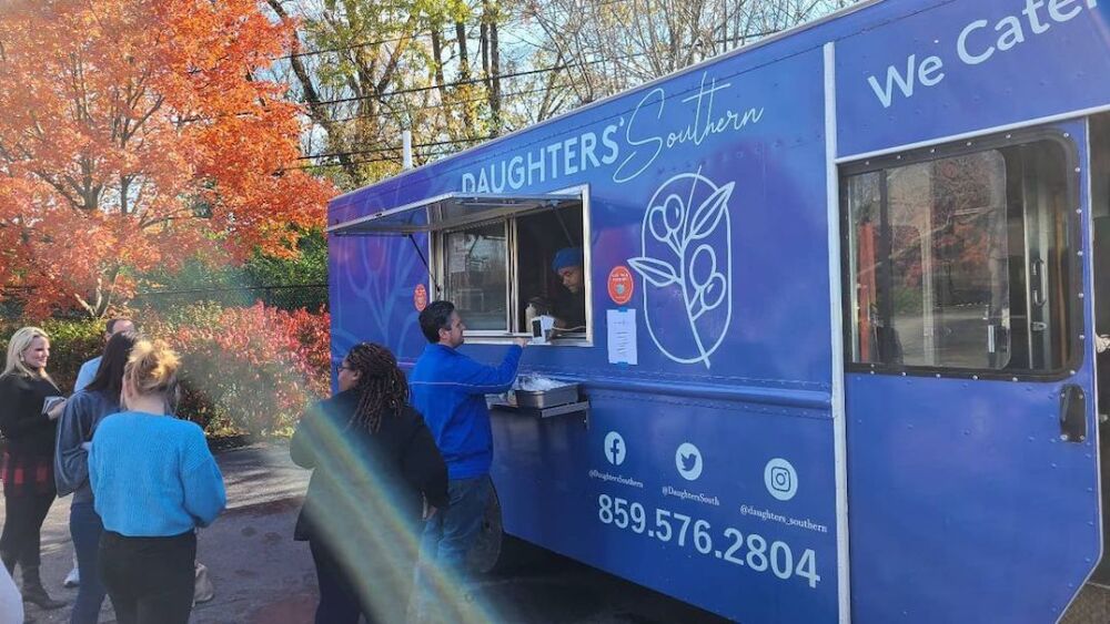 A blue food truck with people lined up outside