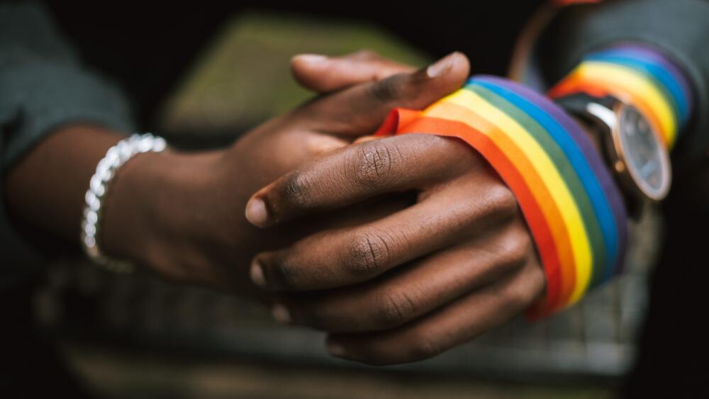 A set of clasped hands with a rainbow ribbon wrapped around one in the forefront.