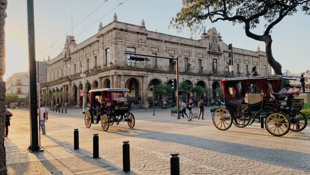Electric carriages roll down a street surrounded by colonial buildings