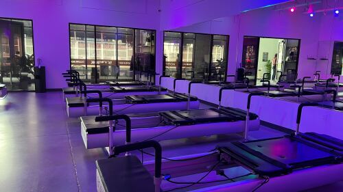 The interior of BODYROK. There are pilates machines and blueish purple lighting inside, with a mirror lining the wall.