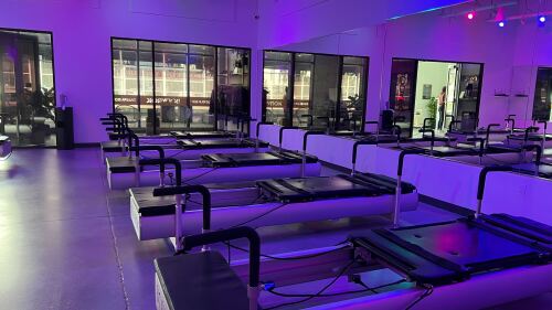 The interior of BODYROK. There are pilates machines and blueish purple lighting inside, with a mirror lining the wall. 