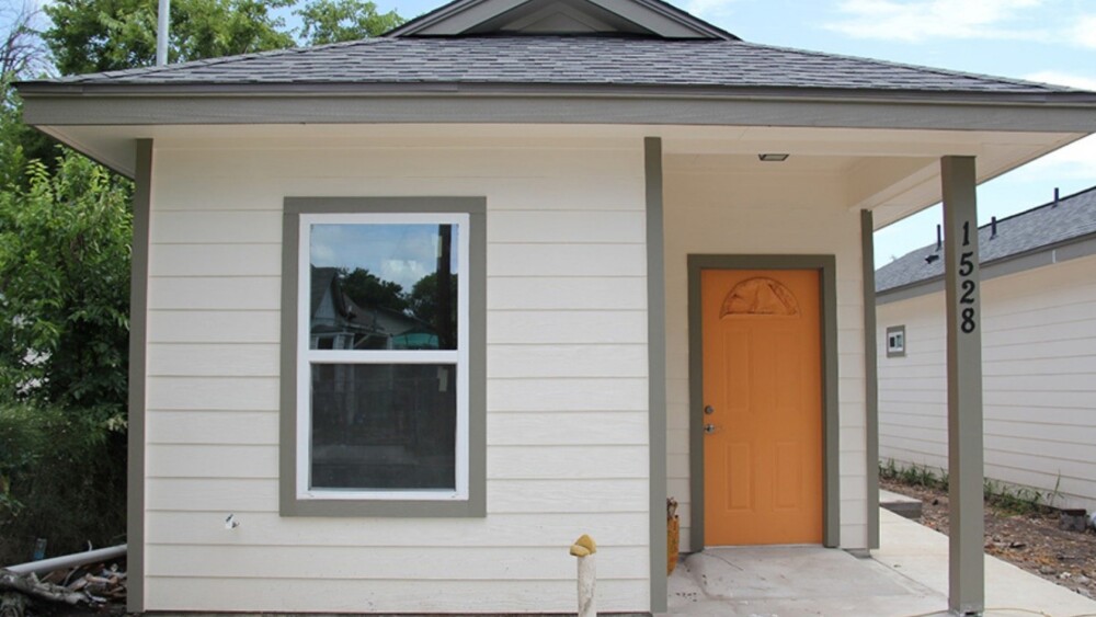 White building with an orange door and grey accent support beams.