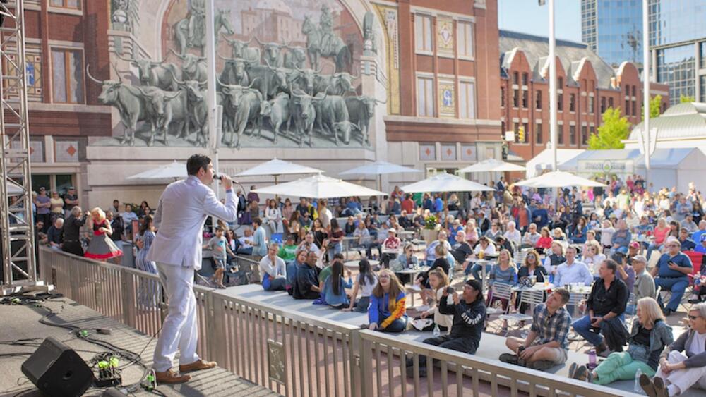 Photo of a person in a white suit performing on stage in front of a crowd in Sundance Square.