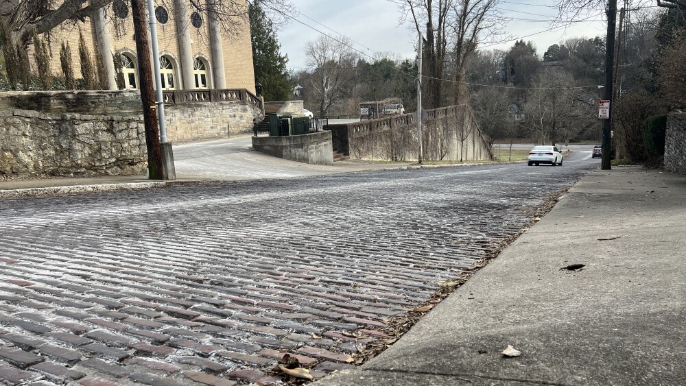 Brick street on a slope with a white care driving down.