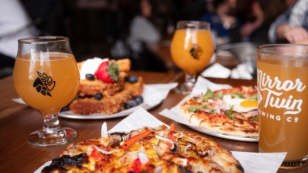 Three plates of food — one with pizza, one with french toast, and one with a pizza topped with an egg — sit on a table surrounded by drinks.