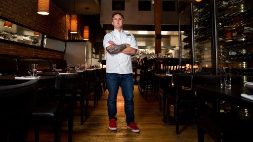Chef Troy Guard poses for the camera in the center of an empty steak restaurant.