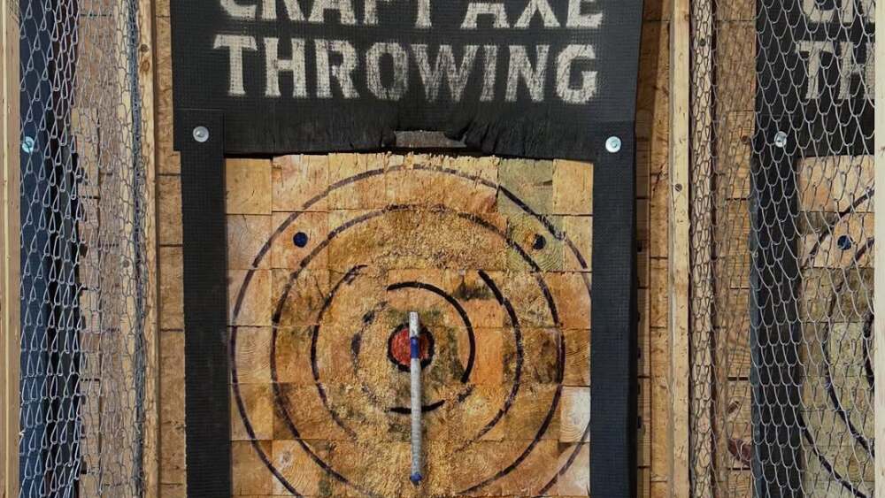 A small axe embedded in the bullseye at a throwing range.