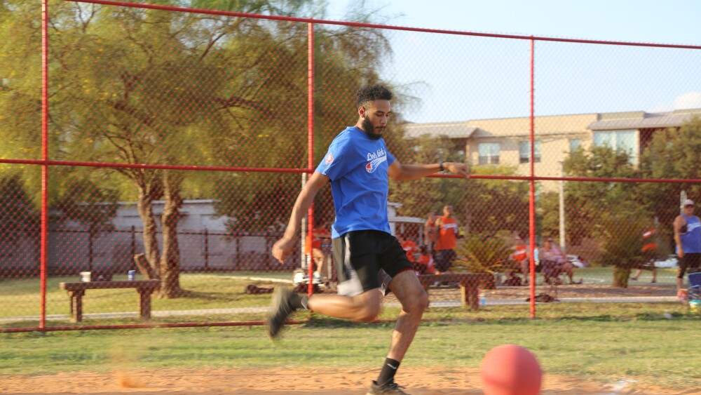 Kickball player kicking a red ball on a baseball field.