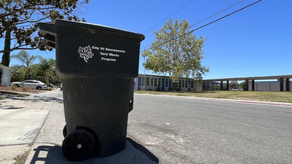 A city waste bin is seen in the middle of the street.