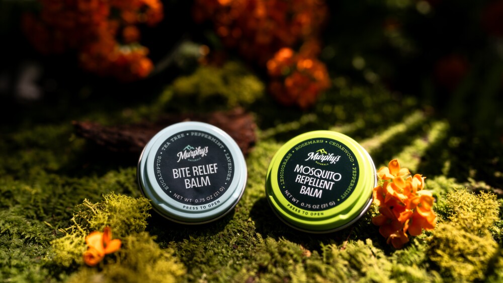 Two Murphy's Naturals balm tins sitting on moss in a forest.