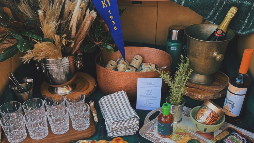 A tailgate set up with glasses, trays of bitesized snacks + bourbon
