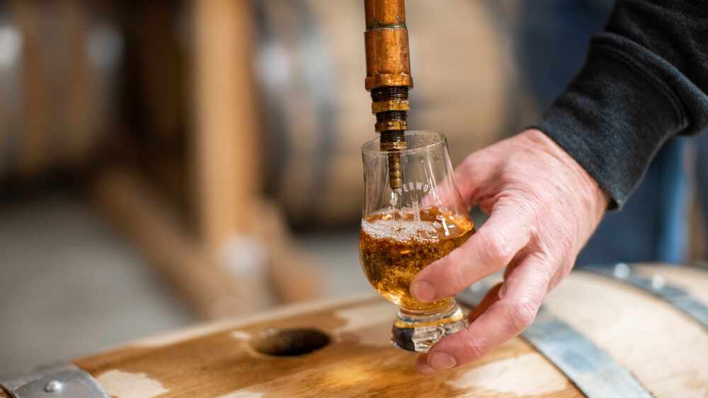 Someone fills a glass with Copperworks Whiskey directly from a barrel.