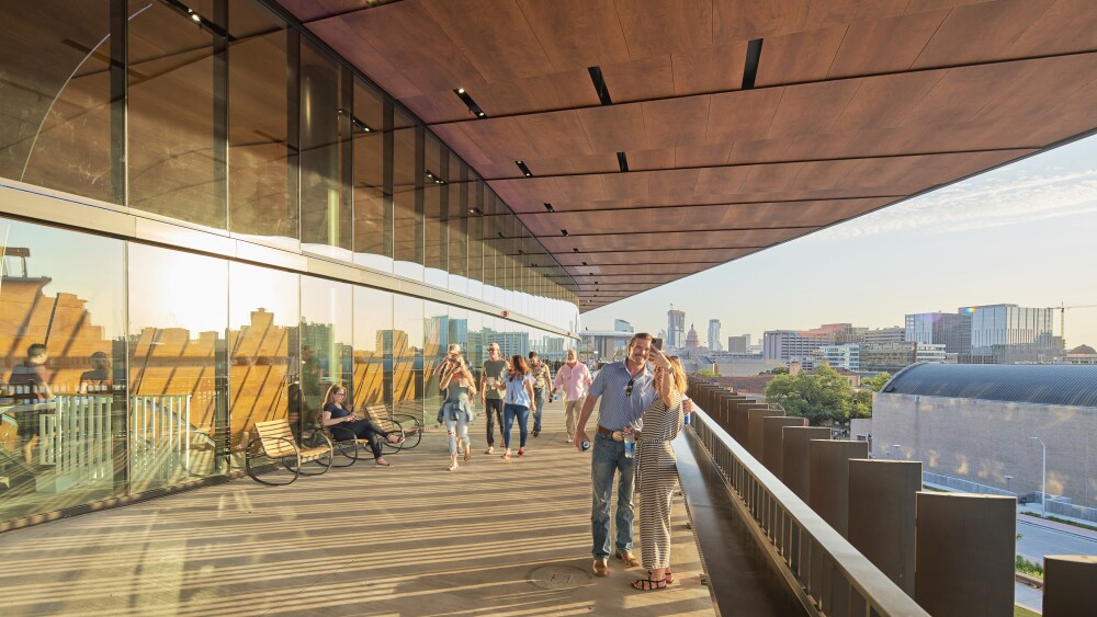 A couple standing on the balcony at the Moody Center, with the Austin skyline in the background.