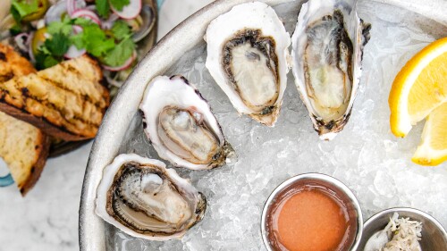 Halved oysters and a few lemon wedges sit on a bed of crushed ice next to some steamed clams that are on a separate dish.
