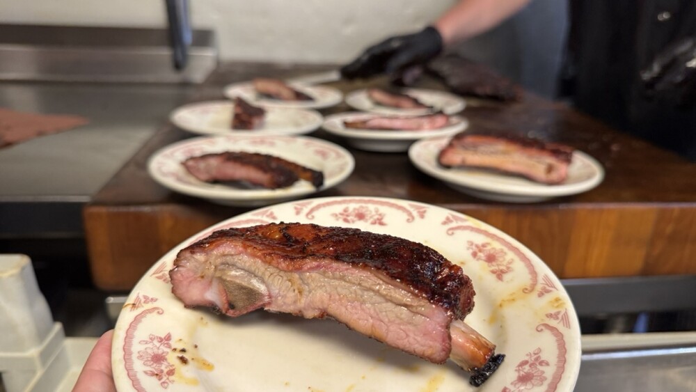 A plate with a pork rib with a slab of cut ribs behind.