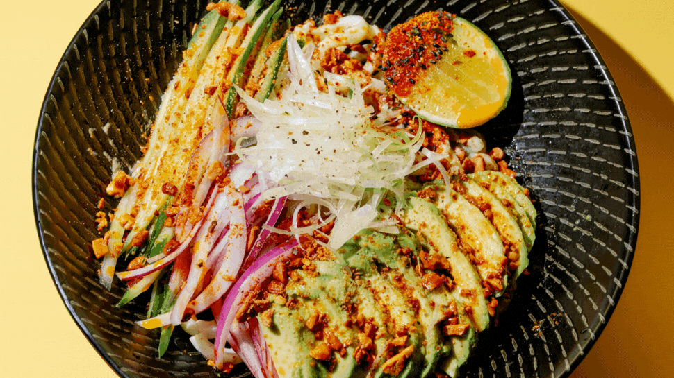Photo 1: A bowl of ramen topped with avocado, onion, cucumbers, lime, and spices. Photo 2: A dish with shrimp + grits artfully plated.